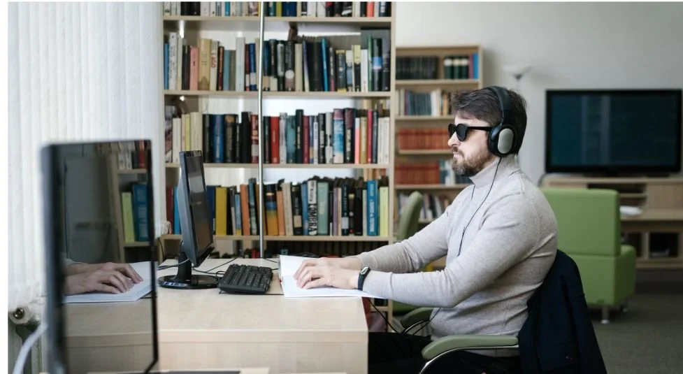 Professional using a computer and headphones in a library workspace.